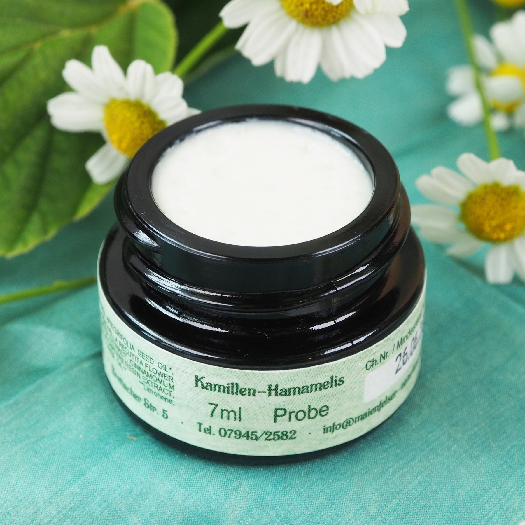 Geöffneter 7ml Kamillen-Hamamelis Creme Tiegel. Kamillenblüten im Hintergrund.